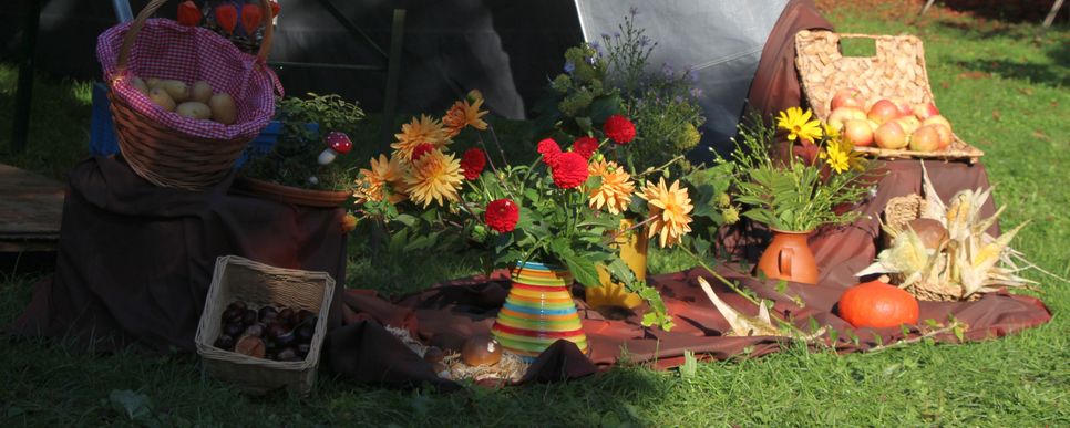 Ein liebevoll gestalteter Erntedanktisch im Freien mit bunten Blumen, Körben voller Äpfel, Kartoffeln, Mais und Kürbis.