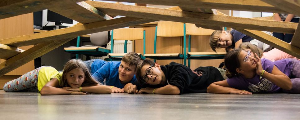 Foto: Wischenbart, KJSÖ Sechs Kinder liegen auf dem Boden unter einer Holzkonstruktion.