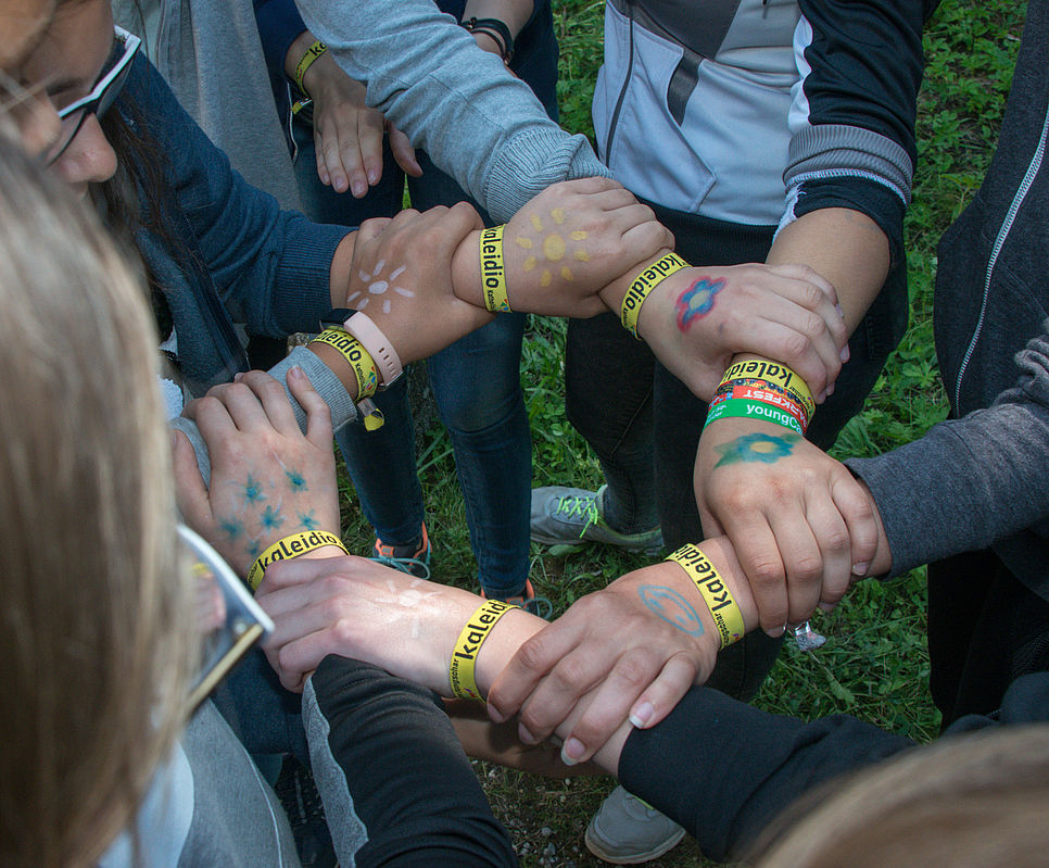 Mehrere Kinder und Jugendliche stehen im Kreis und halten sich gegenseitig an den Unterarmen fest.