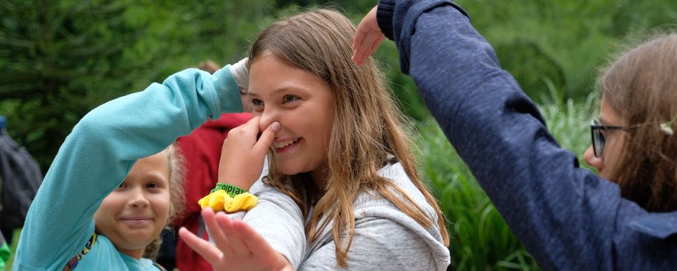 Mädchen lacht und hält sich die Nase zu. Zwei andere Kinder formen ein Herz.