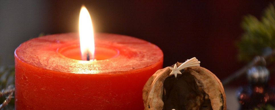 Eine brennende rote Kerze mit einer kleinen Krippe daneben.
