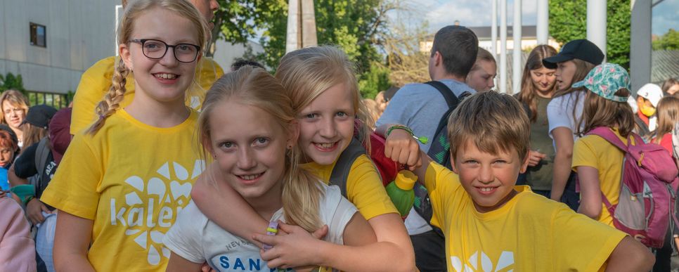 Vier Kinder in gelben Shirts lachen in die Kamera und umarmen sich.