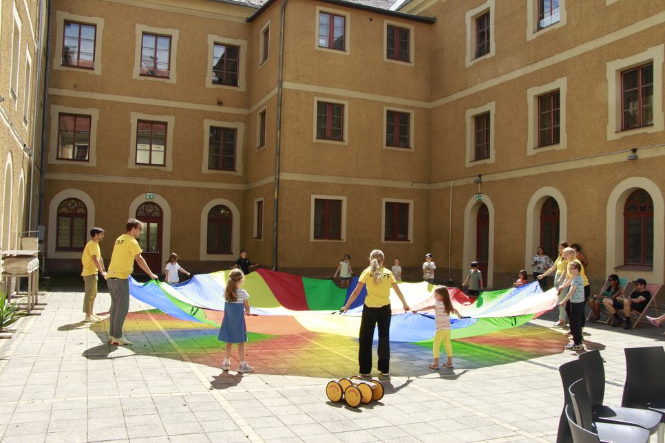 Kindergruppe steht um einen bunten Fallschirm.