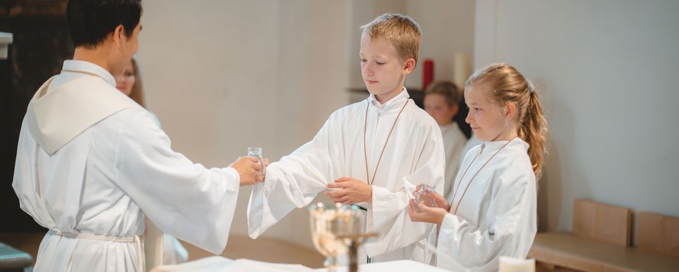 Zwei Ministranten reichen dem Pfarrer bei der Messe ein Gefäß mit Wein.