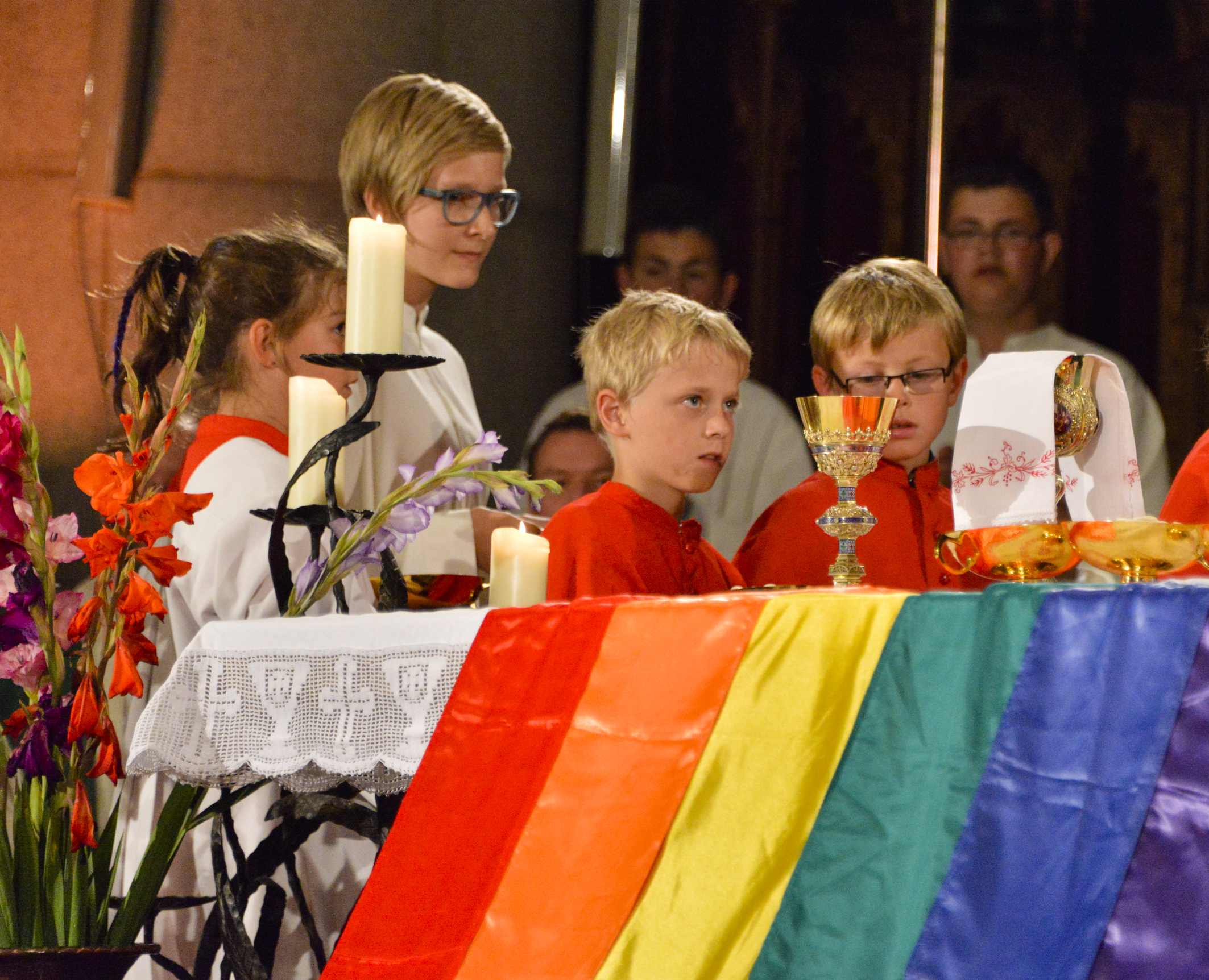 Regenbogenfahne und Kinder sind vor einem Altar zu sehen.